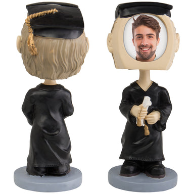 A photo bobble head display featuring a figure in a graduation gown and cap, holding a diploma, with a slot on the top for inserting a photo.