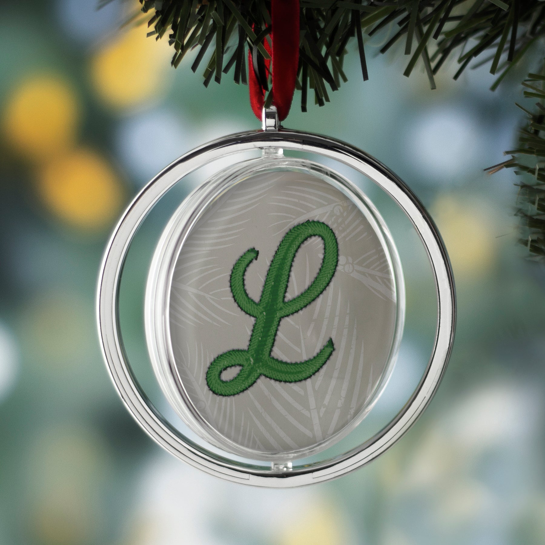 One round, silver photo ornament with a red velvet string at the top hanging on a Christmas tree.