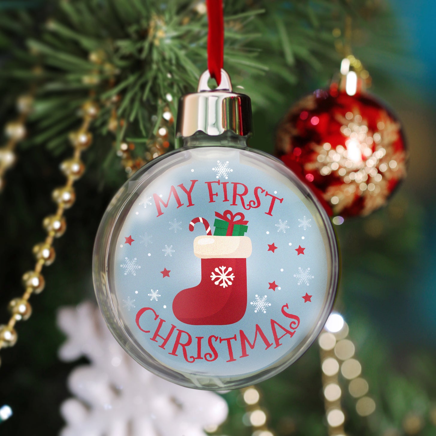 A clear, round Christmas ornament with a photo of a holiday insert, and a red velvet hanger ribbon hanging from a Christmas tree displayed on a festive lifestyle background.