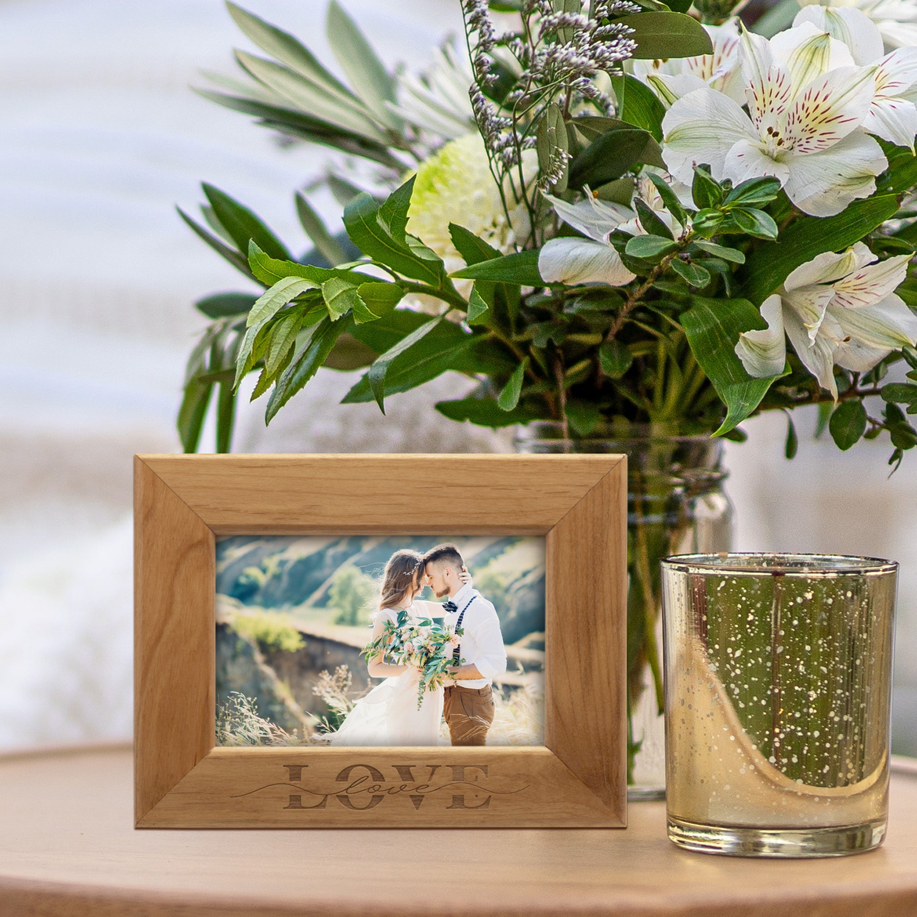 Brown wood picture frame with the text "LOVE" engraved along the bottom shown in a home setting on a table with flowers and a candle.