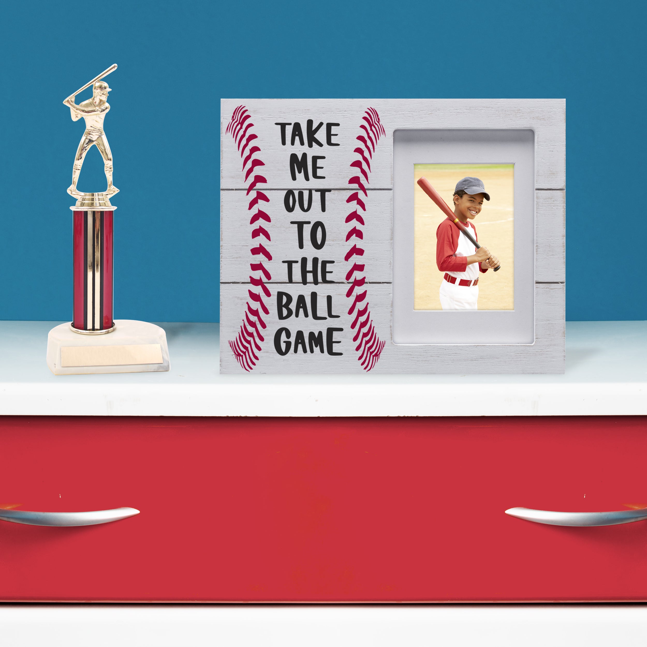 Baseball themed picture frame placed on a dresser in a bedroom with a baseball trophy.