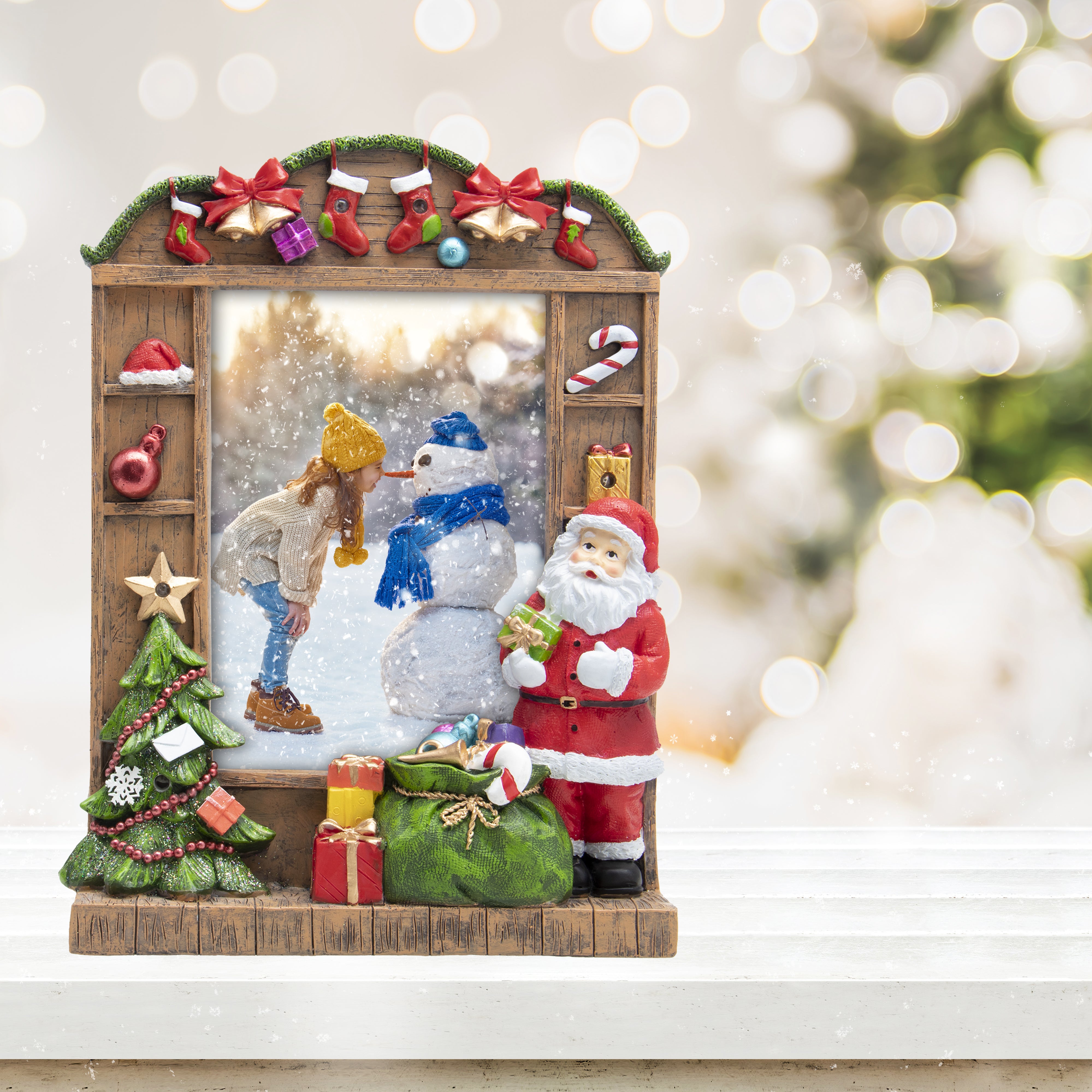 A resin picture frame with a Christmas theme, featuring Santa Claus, a Christmas tree, and wrapped presents. The frame is designed to hold a 5" x 7" photo and has multicolored lights along its border on a festive lifestyle background.