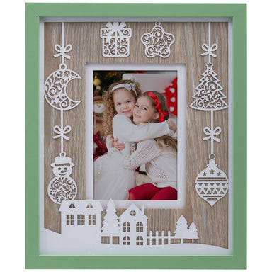 A wooden picture frame with a green border, featuring white laser cut designs including ornaments and houses with trees.