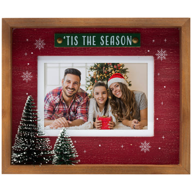 A wooden picture frame with a red background featuring white snowflakes and the text 'Tis the Season'. The frame contains a photo of a family and has two 3D Christmas trees at the bottom.