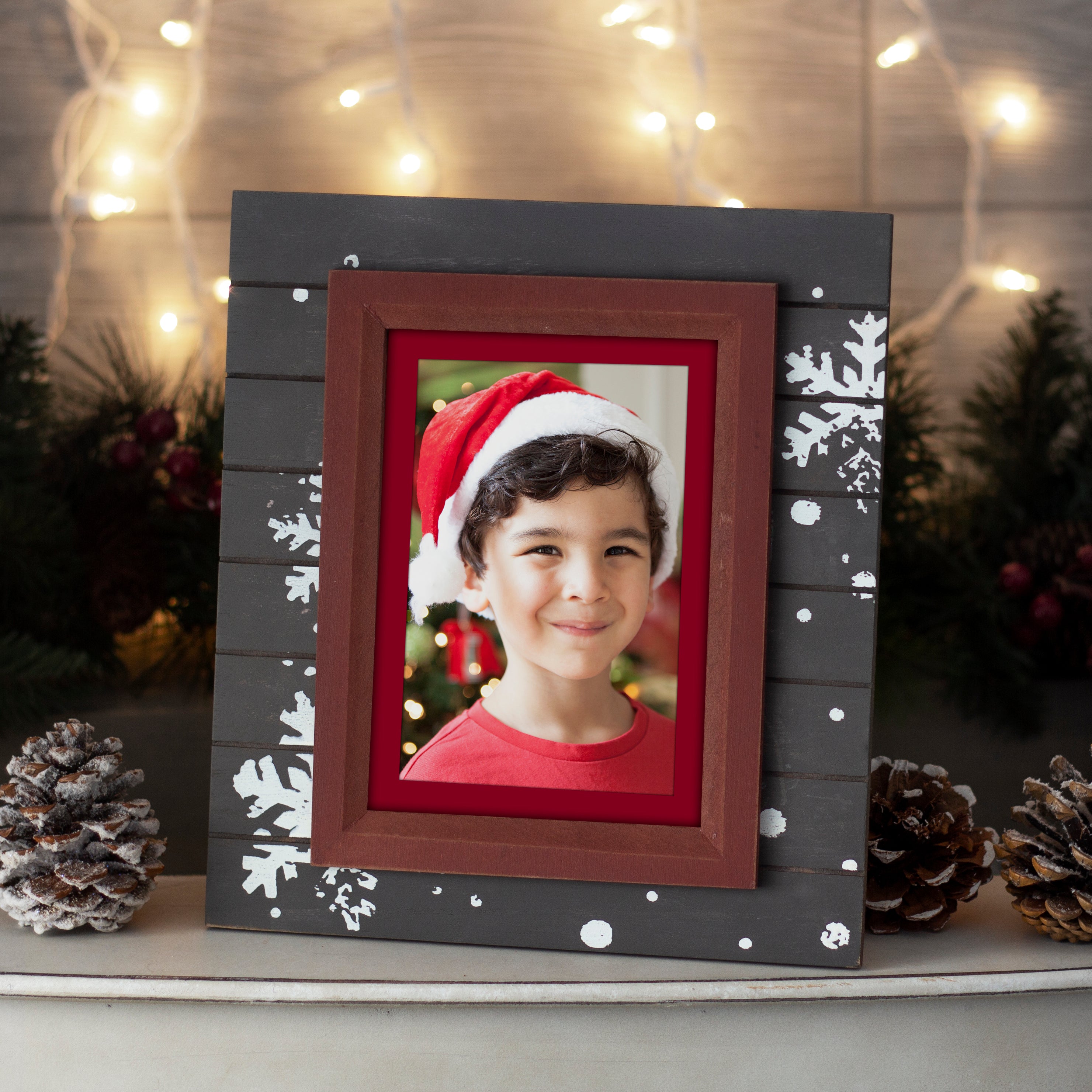 A rectangular brown wood picture frame with a rustic finish. The frame is adorned with white snowflake designs on the brown section. This picture frame is shown in a home setting on a mantel or shelf.