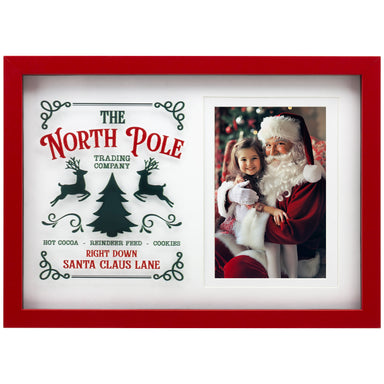 A wooden picture frame with a red border, featuring a photo of a young girl and Santa Claus, and text that reads 'The North Pole Trading Company, Hot Cocoa, Reindeer Food, Cookies, Santa Claus Lane'.