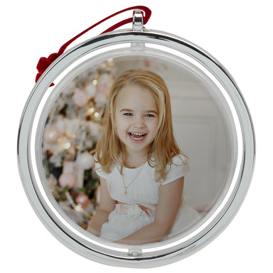 A round, silver photo ornament with a red velvet string at the top on a white background.