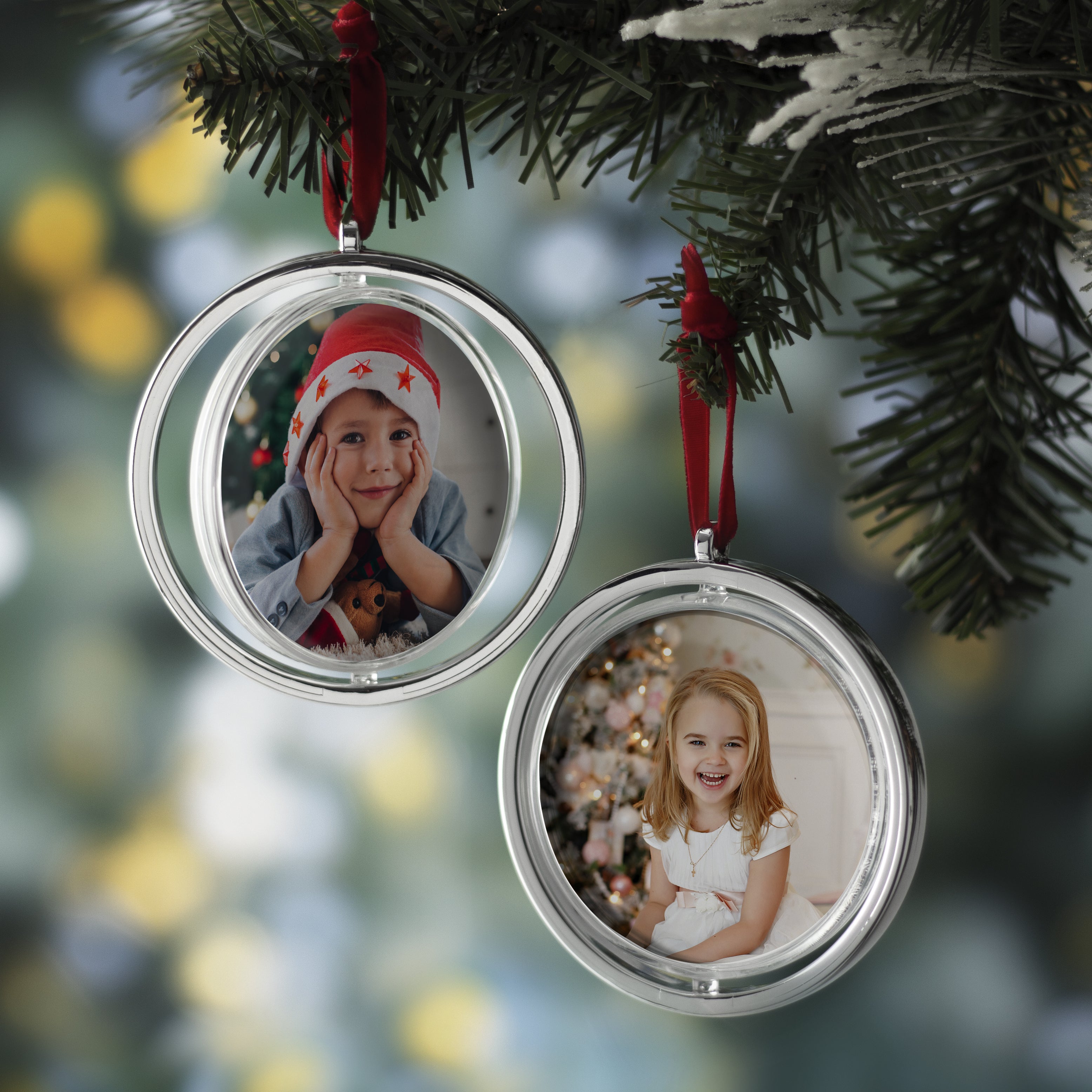 Two round, silver photo ornaments with a red velvet string at the top hanging on a Christmas tree.
