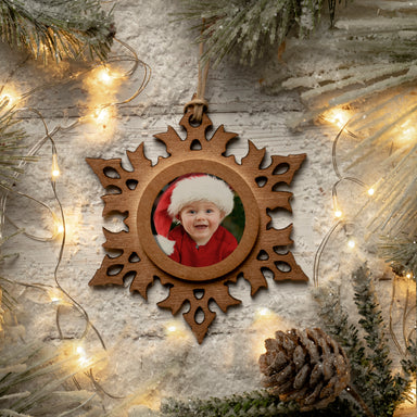 A wooden snowflake-shaped photo ornament with a photo of a smiling child in the center, displayed against a festive lifestyle background.