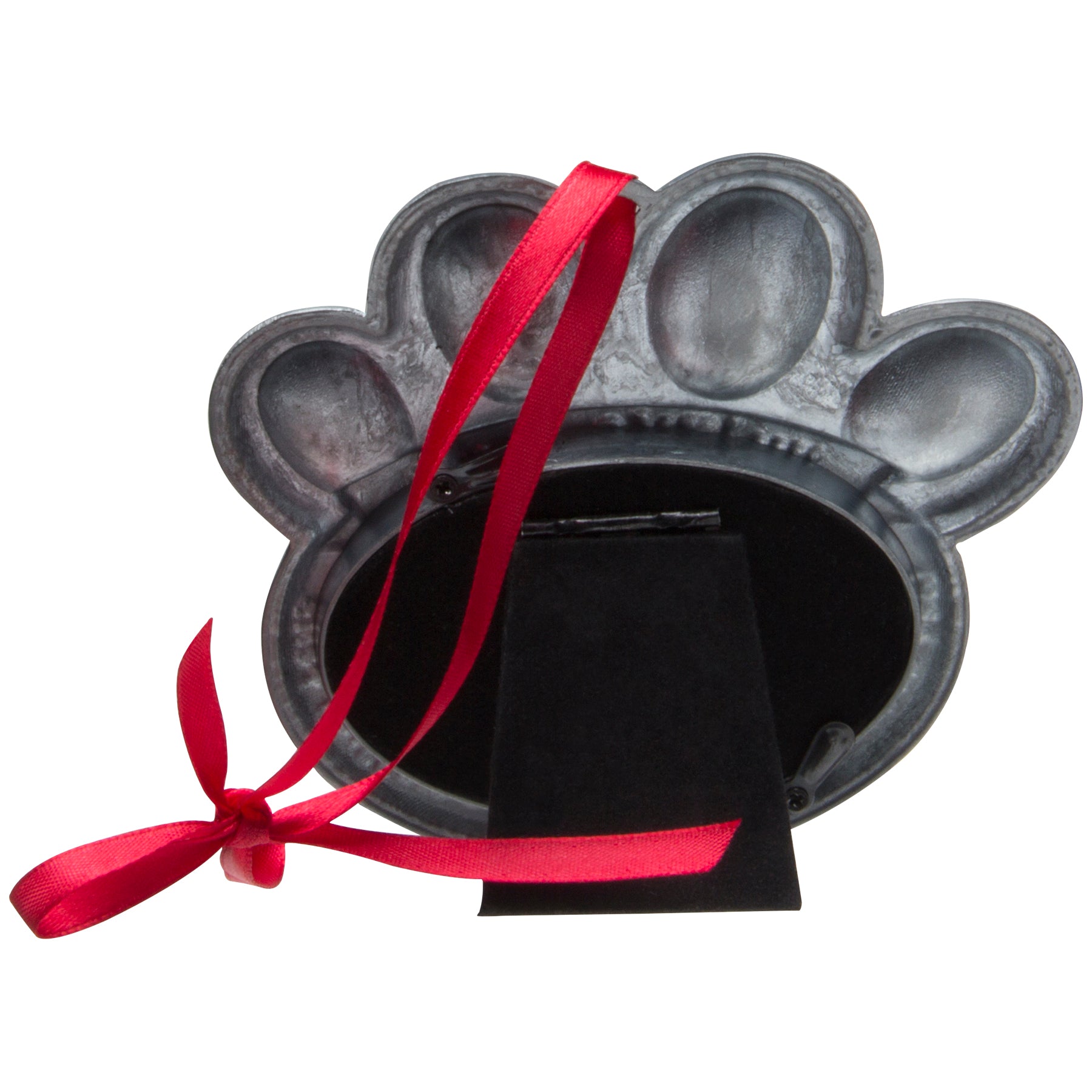 The back side of a pewter ornament shaped like a paw print showcasing the velvet easel for tabletop display as well as a red velvet ribbon to hand from the Christmas tree displayed on a white background.