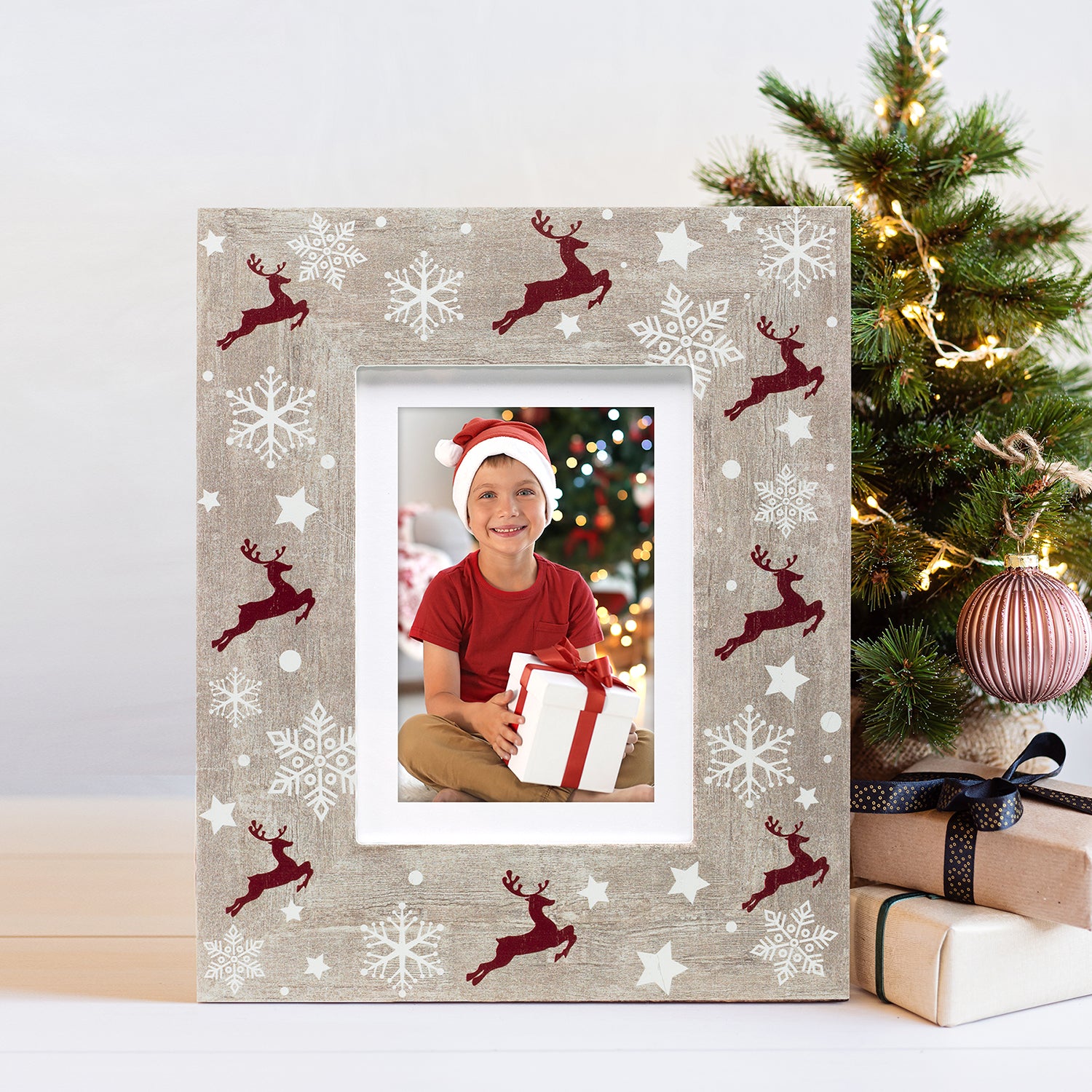 A rustic wooden picture frame with a reindeer and Christmas-themed pattern, displaying a photo of a person wearing a Santa hat on a festive lifestyle background.