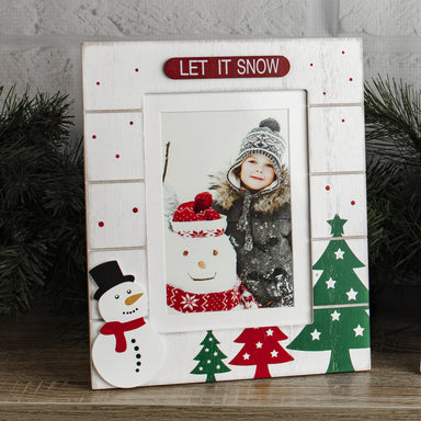 A white, wooden picture frame with a 'LET IT SNOW' sign at the top, and designs featuring Christmas trees, and and a snowman on a festive lifestyle background.