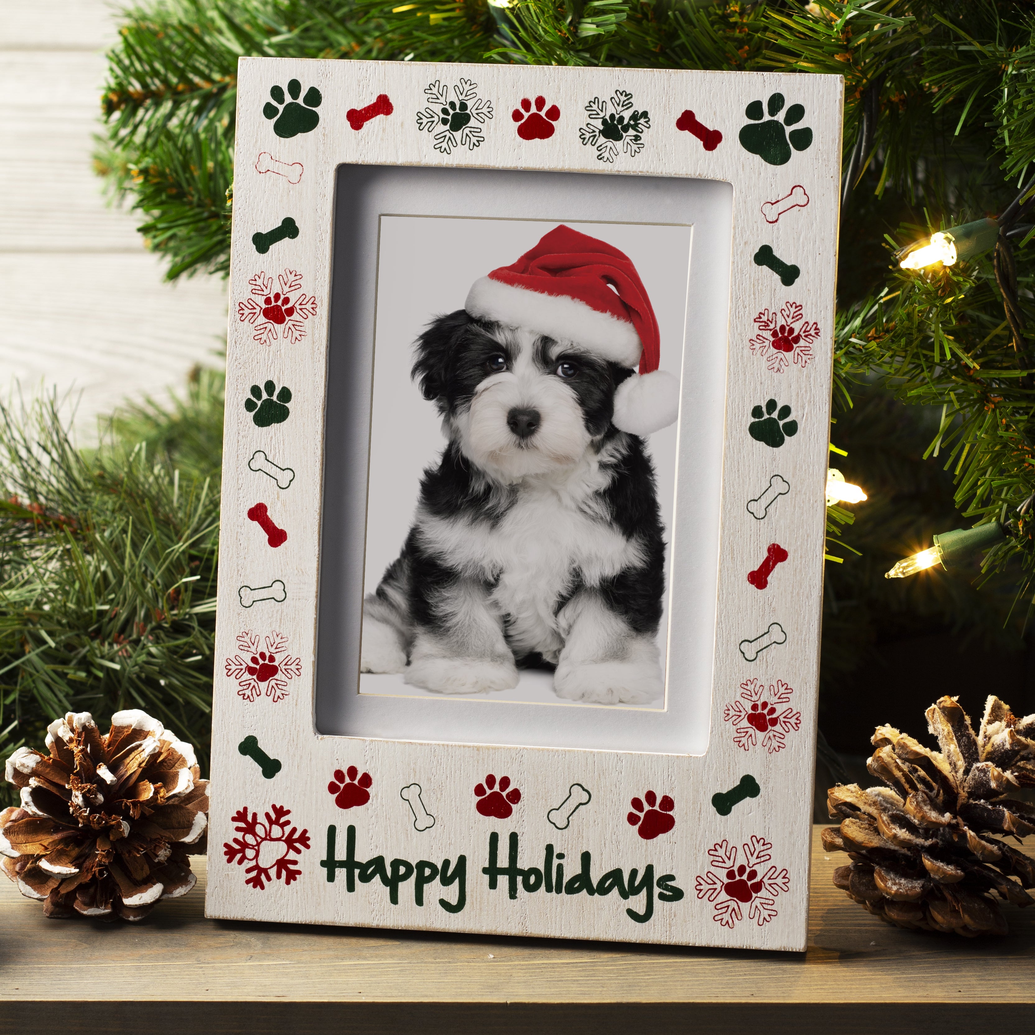 A white wooden picture frame with the phrase "Happy Holidays" at the bottom with a border of paw prints, bones, and snowflakes displayed on a festive lifestyle background.