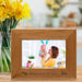 Wooden photo frame with 'Snuggle Bunny' engraving displaying a photo of a woman and child, next to a vase of yellow flowers.