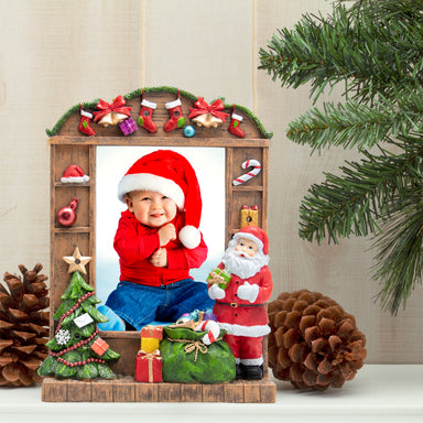 A resin picture frame with a Christmas theme, featuring Santa Claus, a Christmas tree, and wrapped presents. The frame is designed to hold a 5" x 7" photo and has multicolored lights along its border on a festive lifestyle background.